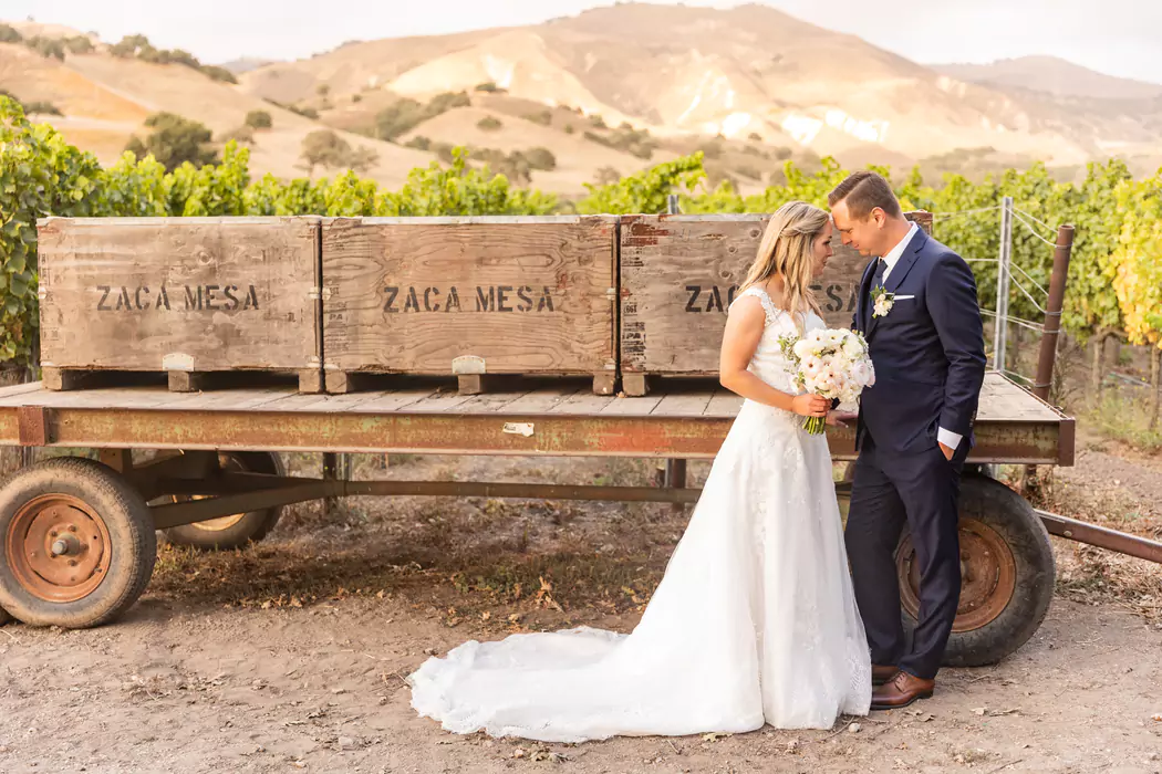 bride and groom touching foreheads in front of a wagon carrying wood wine boxes at Zaca Mesa in Santa Barbara