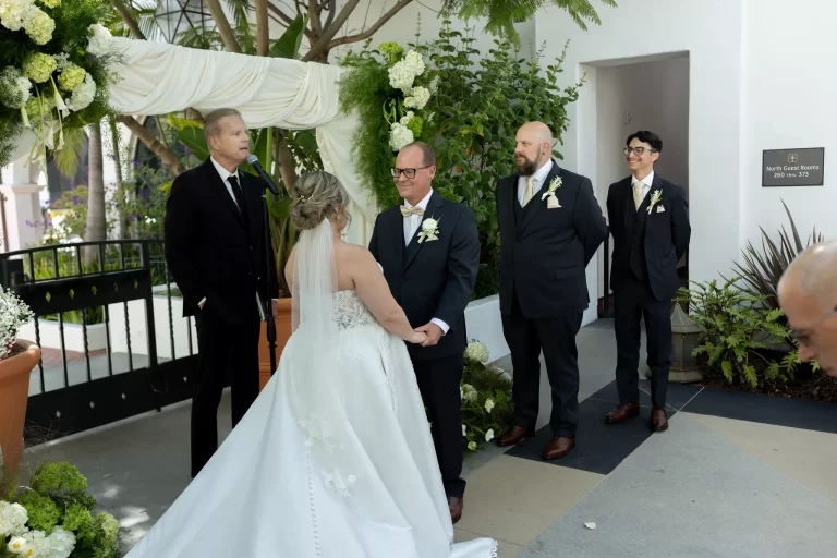 Bride and groom exchange vows beneath floral wedding arch